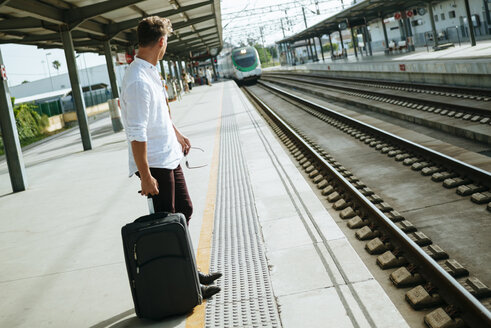 Junger Mann mit Koffer wartet am Bahnsteig - KIJF000564