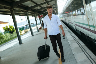 Young man with suitcase walking at station platform - KIJF000565