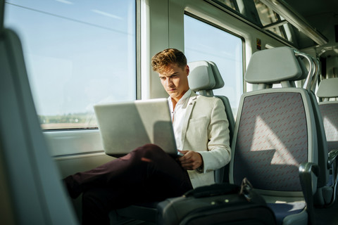Junger Mann benutzt einen Laptop im Zug, lizenzfreies Stockfoto