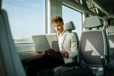 Young man using a laptop on a train - KIJF000570