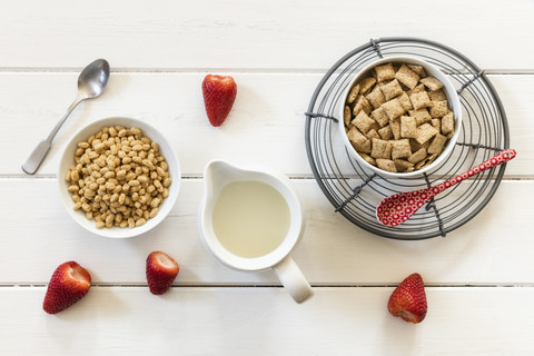 Schüsseln mit Hafervollkornkissen und Haferflocken, Erdbeeren und ein Milchkännchen, lizenzfreies Stockfoto