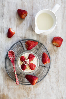 Glass of overnight oats with strawberries and milk jug on wood - EVGF003022