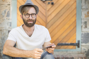 Bearded man outdoors with cell phone wearing hat and glasses - ZEF008979