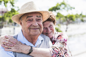 Porträt eines glücklichen Seniors mit seiner lächelnden Frau im Hintergrund - UUF008037