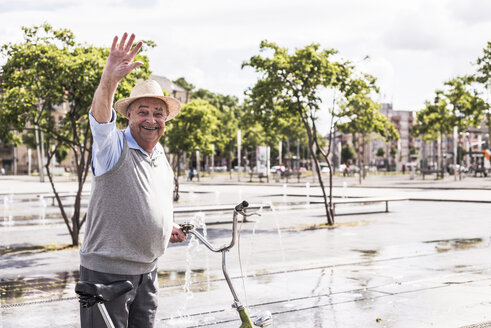 Portrait of waving senior man with folding bicycle - UUF008044