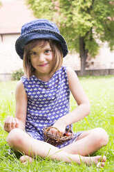 Portrait of little girl sitting on a meadow with basket of gooseberries - LVF005116