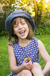 Portrait of laughing little girl sitting on a meadow with gooseberry - LVF005118