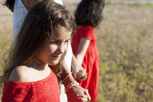 Porträt eines lächelnden kleinen Mädchens, das Hand in Hand mit seiner Mutter und seiner Schwester geht - VABF000671
