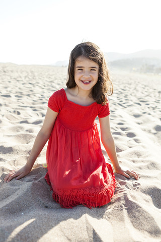 Porträt eines lächelnden kleinen Mädchens, das am Strand kniet, lizenzfreies Stockfoto