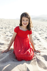 Porträt eines lächelnden kleinen Mädchens, das am Strand kniet - VABF000676