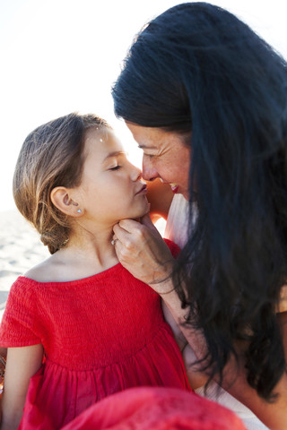 Mother and little daughter sitting on the beach rubbing noses stock photo