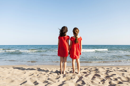 Rückenansicht von zwei kleinen Schwestern, die am Strand stehen und auf das Meer schauen - VABF000681