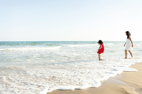 Kleines Mädchen und ihre Mutter gehen am Strand spazieren, lizenzfreies Stockfoto