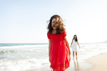 Glückliches kleines Mädchen am Strand mit ihrer Mutter im Hintergrund - VABF000684