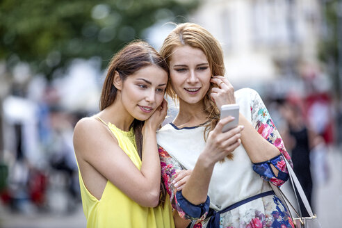 Zwei junge Frauen schauen auf ein Handy in der Stadt - GDF001052