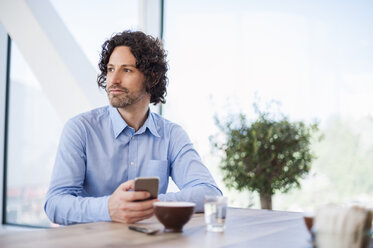 Portrait of man with smartphone and cup of Cappuccino looking at distance - DIGF000567