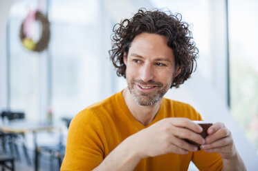Porträt eines lächelnden Mannes mit lockigem braunem Haar, der eine Tasse Kaffee hält - DIGF000569