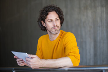 Portrait of pensive man with curly brown hair holding tablet looking at distance - DIGF000576