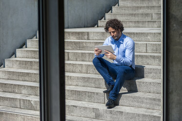 Geschäftsmann sitzt auf einer Treppe und schaut auf ein Tablet - DIGF000583