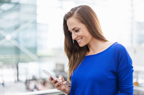 Lächelnde brünette Frau schaut auf ihr Handy, lizenzfreies Stockfoto