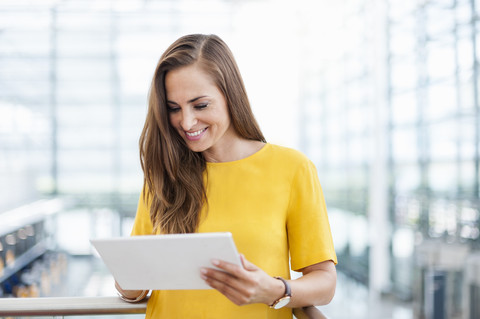 Lächelnde brünette Frau schaut auf ein digitales Tablet, lizenzfreies Stockfoto