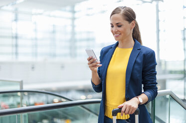 Lächelnde Frau an einem Bahnhof, die auf ihr Handy schaut - DIGF000609