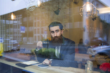 Modischer Mann mit Bart sitzt in einem Café und trinkt Kaffee - NAF000011