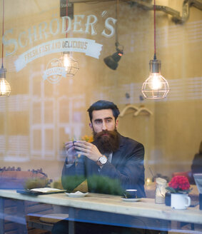 Modischer Mann mit Bart sitzt in einem Café und trinkt Kaffee - NAF000012