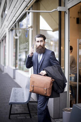 Hipster with briefcase and smart phone leaving coffee shop - NAF000014