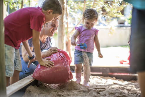 Familie füllt Sand in den Sandkasten - ZEF009025