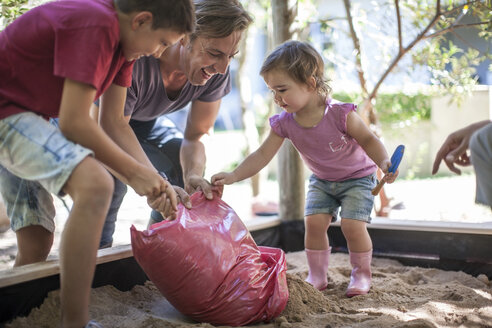 Familie füllt Sand in den Sandkasten - ZEF009026