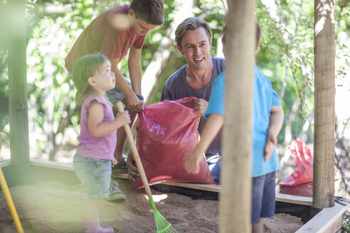 Familie füllt Sand in den Sandkasten - ZEF009029