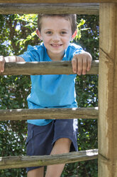 Porträt eines lächelnden Jungen auf einem Spielplatz, der eine Leiter hochklettert - ZEF009033