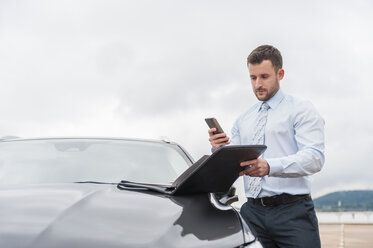 Geschäftsmann mit Dokumenten und Mobiltelefon am Auto - DIGF000644