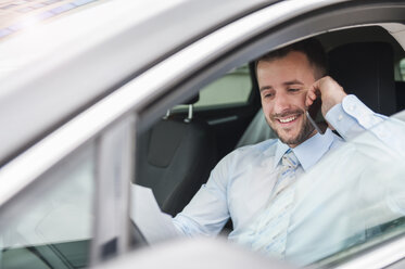 Lächelnder Geschäftsmann mit Dokumenten auf einem Mobiltelefon im Auto - DIGF000646