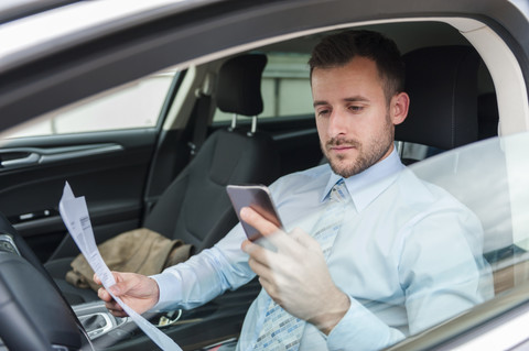 Geschäftsmann mit Dokumenten und Mobiltelefon im Auto, lizenzfreies Stockfoto