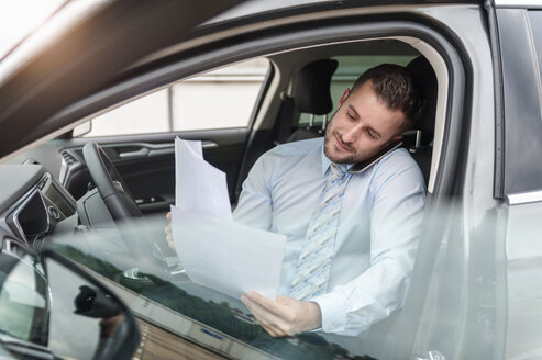 Businessman with documents on cell phone in car - DIGF000650