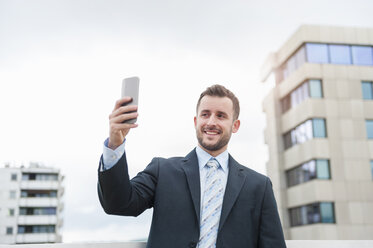 Lächelnder Geschäftsmann macht ein Selfie vor einem Bürogebäude - DIGF000655