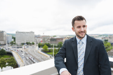 Smiling businessman on roof terrace above the city - DIGF000657