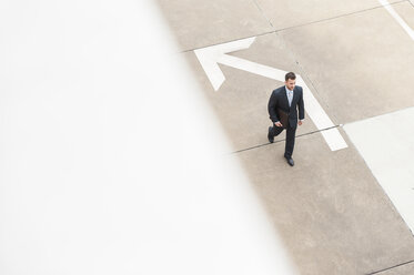 Businessman walking on paving with large arrow - DIGF000661