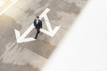 Businessman walking on paving with large arrow - DIGF000662