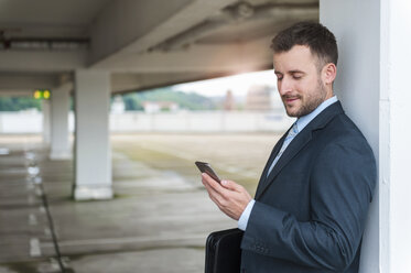 Businessman looking at cell phone in parking garage - DIGF000665