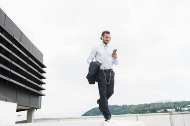 Happy businessman wearing headphones balancing on wall - DIGF000670