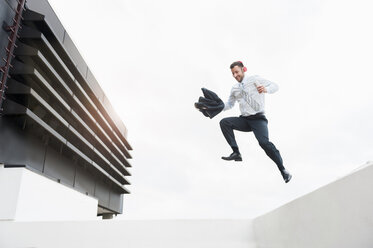 Happy businessman wearing headphones jumping from wall - DIGF000671