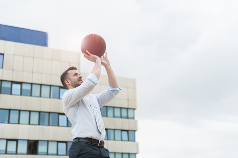 Businessman playing basketball outdoors stock photo