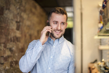 Lächelnder junger Mann, der in einem Geschäft mit seinem Handy telefoniert - DIGF000679