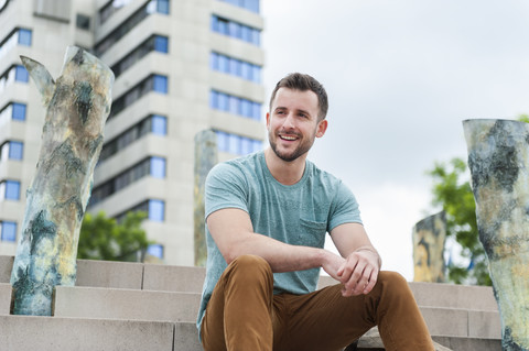 Smiling young man outdoors sitting on stairs stock photo