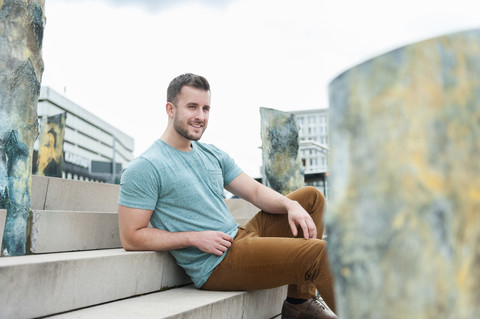 Lächelnder junger Mann im Freien auf einer Treppe sitzend, lizenzfreies Stockfoto