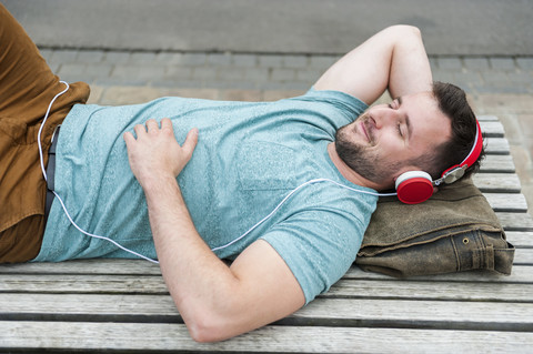 Relaxed young man lying on bench listening to music stock photo