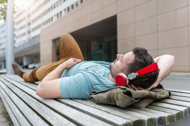 Entspannter junger Mann liegt auf einer Bank und hört Musik - DIGF000699